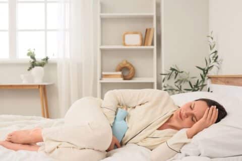 Mulher deitada na cama com bolsa térmica no abdômen, imagem ilustrativa de dor associada à endometriose