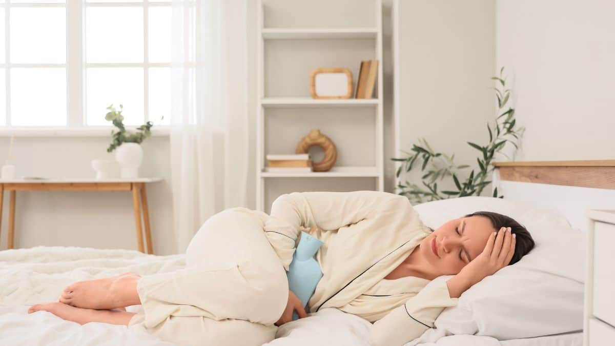 Mulher deitada na cama com bolsa térmica no abdômen, imagem ilustrativa de dor associada à endometriose